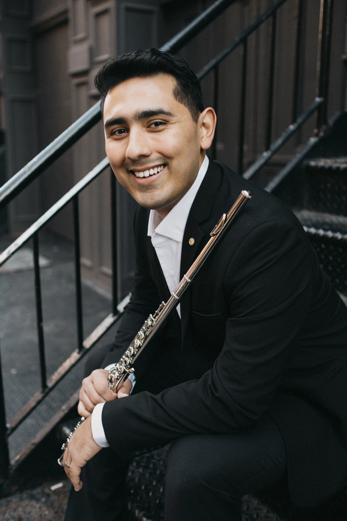 Saqtiel smiling with his flute while seated on a New York stoop