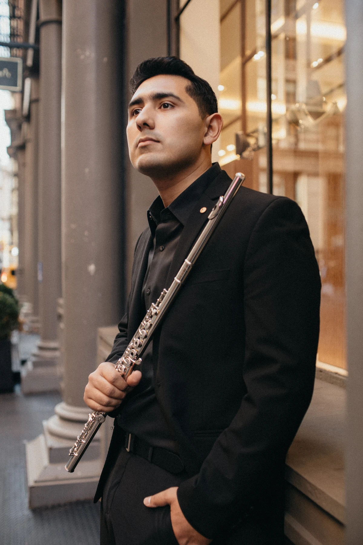 Saqtiel holding his flute beside a warmly lit storefront