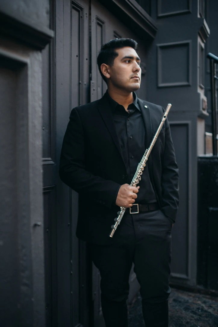 Saqtiel holding his flute diagonally beside a dark doorway