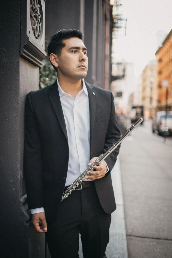 Saqtiel holding his flute beside an ornate column on a city sidewalk